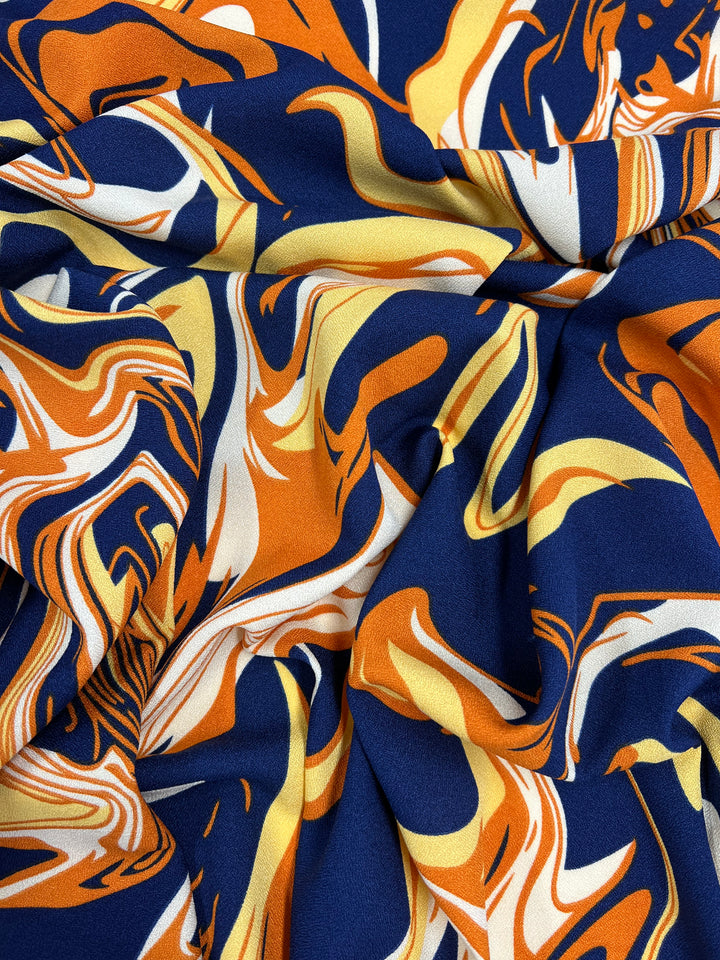 The Printed Crepe - Potion by Super Cheap Fabrics is a luxurious fabric featuring a swirl pattern in bold orange, navy blue, yellow, and white. Its dynamic design creates fluid, wave-like shapes that add movement and texture to the 150cm material.