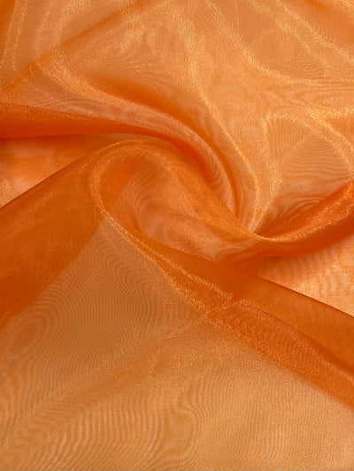 A close-up of Super Cheap Fabrics' Organza in Orange, measuring 150cm, softly draped in a translucent hue. This lightweight fabric catches the light beautifully, creating a subtle sheen and gentle waves.