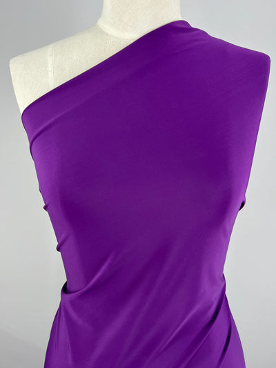 A mannequin is draped in a vibrant purple, single-shoulder garment made of Super Cheap Fabrics' medium-weight Nylon Lycra, measuring 160cm in width, shown against a plain background. The fabric appears smooth with a slight sheen, elegantly wrapping around the mannequin's torso.