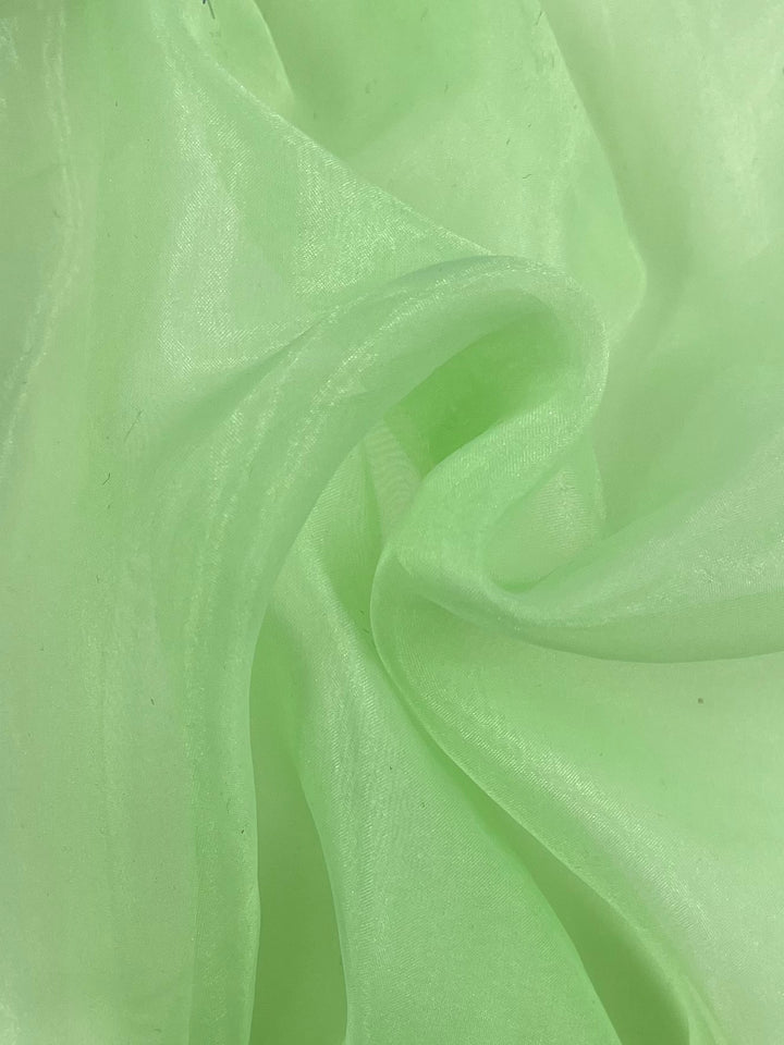 A close-up image of a gently folded sheer Organza - Ambrosia fabric in light green. This 100% polyester, lightweight fabric from Super Cheap Fabrics has a soft, flowing texture with a subtle shine, creating a delicate and smooth appearance.